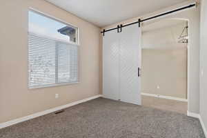 Unfurnished bedroom featuring a barn door and carpet floors