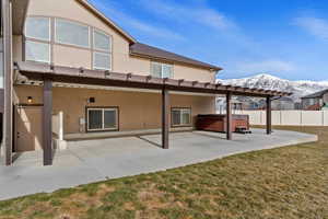 Rear view of property with a mountain view, a yard, a patio, and a hot tub