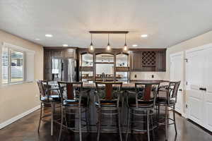 Kitchen featuring pendant lighting, stainless steel fridge with ice dispenser, a kitchen island, a kitchen bar, and dark brown cabinetry