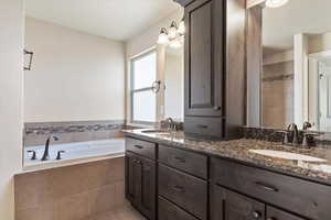 Bathroom featuring tile patterned floors, vanity, and a relaxing tiled tub