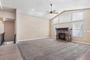 Unfurnished living room featuring ceiling fan, a fireplace, and vaulted ceiling