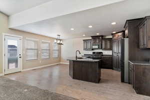 Kitchen featuring pendant lighting, black appliances, a center island with sink, sink, and dark brown cabinetry