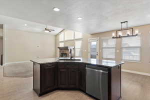 Kitchen with ceiling fan with notable chandelier, a kitchen island with sink, sink, dishwasher, and hanging light fixtures