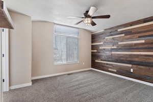 Spare room with carpet, a textured ceiling, ceiling fan, and wooden walls