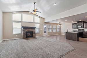 Living room with sink, a stone fireplace, vaulted ceiling, ceiling fan with notable chandelier, and light wood-type flooring