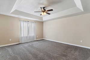 Carpeted spare room featuring a tray ceiling and ceiling fan