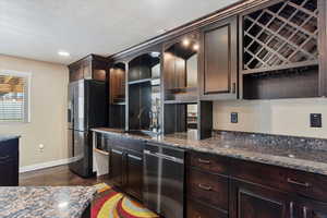 Kitchen with dark brown cabinetry, sink, stainless steel appliances, dark stone counters, and a textured ceiling