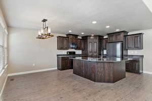 Kitchen with dark brown cabinetry, sink, light hardwood / wood-style flooring, decorative light fixtures, and black appliances