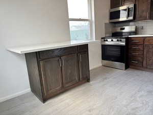 Kitchen with appliances with stainless steel finishes, dark brown cabinetry, and tasteful backsplash