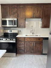 Kitchen with appliances with stainless steel finishes, backsplash, dark brown cabinets, and sink