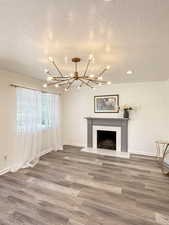 Unfurnished living room with a textured ceiling, a chandelier, wood finished floors, and a premium fireplace