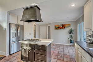 Kitchen with white cabinetry, premium range hood, crown molding, light tile patterned floors, and appliances with stainless steel finishes