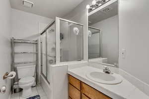 Full bathroom with tile patterned floors, vanity, toilet, and bath / shower combo with glass door