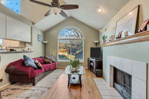 Living room with ceiling fan, vaulted ceiling, light wood-type flooring, and a tiled fireplace