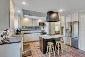 Kitchen featuring sink, stainless steel appliances, a breakfast bar, a kitchen island, and custom range hood