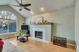 Living room with ceiling fan, light hardwood / wood-style floors, lofted ceiling, and a tile fireplace