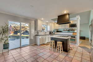 Kitchen with custom exhaust hood, a breakfast bar, stainless steel appliances, a center island, and white cabinetry