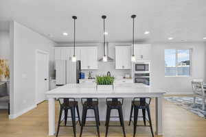 Kitchen with built in microwave, wall chimney range hood, white refrigerator, oven, and white cabinetry