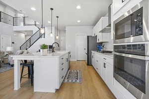 Kitchen with a kitchen island with sink, wall chimney range hood, sink, appliances with stainless steel finishes, and white cabinetry