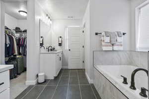 Bathroom with tile patterned flooring, vanity, a relaxing tiled tub, and a textured ceiling