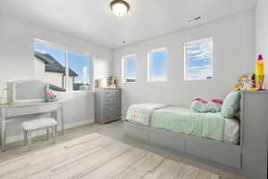 Bedroom with a textured ceiling, light carpet, and multiple windows