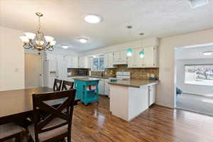 Kitchen with white appliances, white cabinetry, kitchen peninsula, and a wealth of natural light