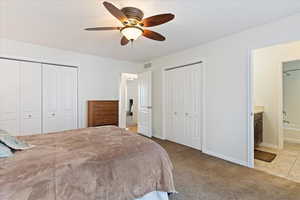 Bedroom with ensuite bath, ceiling fan, light colored carpet, and multiple closets