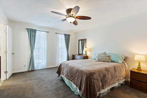 Carpeted bedroom featuring ceiling fan and a textured ceiling