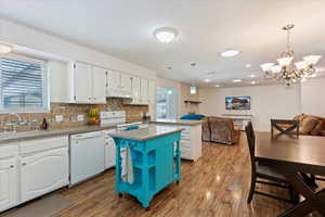 Kitchen with sink, white cabinets, decorative light fixtures, and white appliances