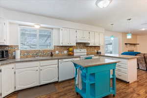 Kitchen with a center island, white cabinets, hanging light fixtures, and white appliances