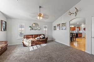 Carpeted living room featuring lofted ceiling, a wealth of natural light, and ceiling fan with notable chandelier