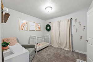 Bedroom with dark colored carpet, a textured ceiling, and a nursery area