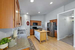 Kitchen featuring sink, wooden counters, a kitchen island, black appliances, and light wood-type flooring