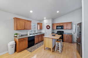 Kitchen with a center island, black appliances, sink, light hardwood / wood-style floors, and a breakfast bar area