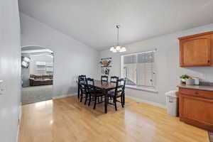 Dining room with ceiling fan with notable chandelier, light hardwood / wood-style floors, and lofted ceiling