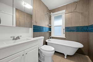 Bathroom featuring tile patterned floors, toilet, a bathtub, vanity, and tile walls