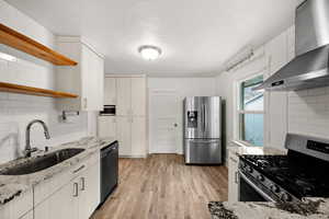 Kitchen with light stone counters, sink, wall chimney range hood, and appliances with stainless steel finishes