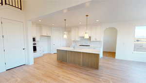 Kitchen with decorative light fixtures, light hardwood / wood-style floors, white cabinets, and a kitchen island with sink