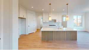 Kitchen featuring decorative light fixtures, an island with sink, decorative backsplash, and white cabinetry