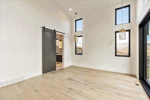 Unfurnished room with a barn door, light hardwood / wood-style floors, and a towering ceiling