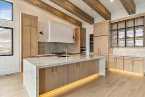 Kitchen featuring tasteful backsplash, light stone counters, oven, a center island with sink, and light wood-type flooring