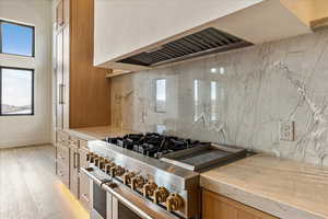 Kitchen with high end stove, tasteful backsplash, light hardwood / wood-style flooring, and custom exhaust hood