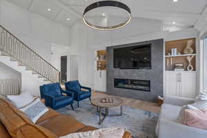 Living room with beam ceiling, wood-type flooring, built in features, and a premium fireplace