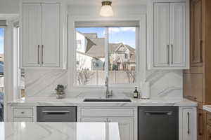 Kitchen featuring light stone countertops, decorative backsplash, white cabinetry, and sink