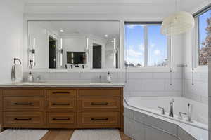 Bathroom featuring tiled bath, crown molding, vanity, and hardwood / wood-style flooring