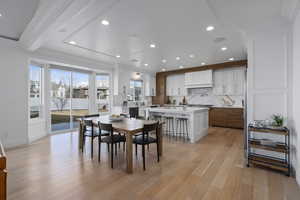 Dining area featuring beam ceiling, sink, light wood-type flooring, and crown molding