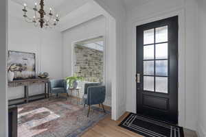 Entryway with crown molding, a chandelier, and light wood-type flooring