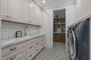 Clothes washing area featuring washer and clothes dryer, sink, cabinets, and ornamental molding