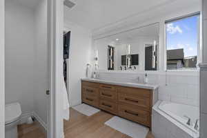 Bathroom with tiled bath, crown molding, hardwood / wood-style floors, toilet, and vanity