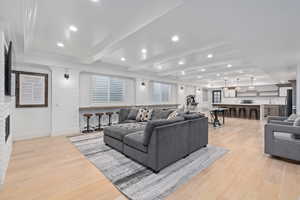 Living room with beam ceiling, light wood-type flooring, a stone fireplace, and sink